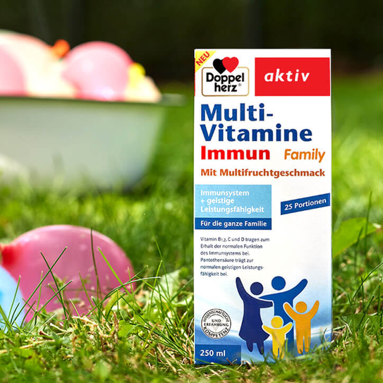 Doppelherz Multi-Vitamine Immun Family steht im Gras, Wasserbomben im Hintergrund